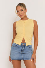Woman wearing a yellow sleeveless top and blue denim skirt against a white background