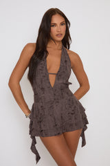A model wearing a brown distressed plunge mini dress with a halter neck.